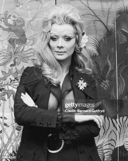 Portrait of Belgian actress Monique Van Vooren as she poses with her arms crossed over a jacket and transparent shirt, 1970s.