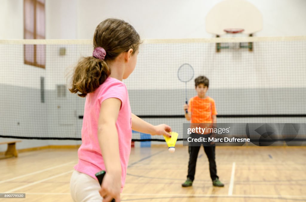 Two kids playing badminton in a gymnasium
