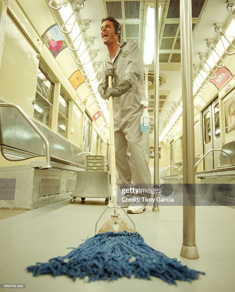 Maintenance worker cleaning subway car, listening to headphones