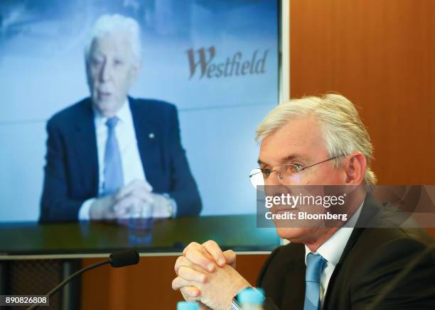 Steven Lowy, co-chief executive officer of Westfield Corp., sits as billionaire Frank Lowy, chairman, is seen on a screen during a news conference in...