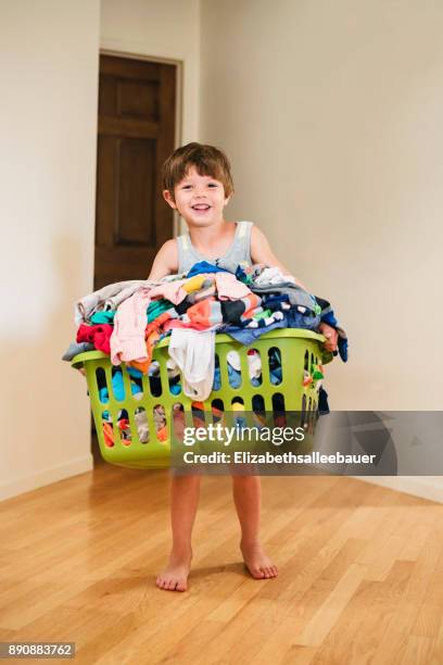 smiling boy carrying laundry basket filled with clothes - laundry basket foto e immagini stock