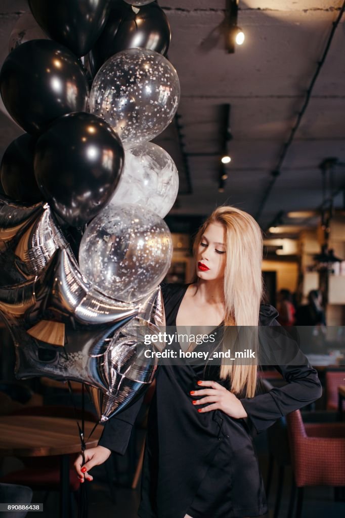 Young woman standing in a cafe holding balloons