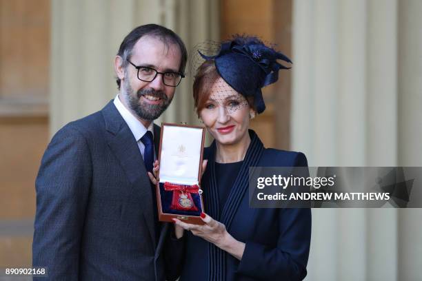 British author JK Rowling, accompanied by her husband Neil Murray, poses with her medal after being made a Companion of Honour for services to...