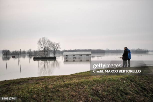 People look out onto a flooded area in Brescello on December 12 after the Enza river broke its banks, following heavy rain throughout the northern...