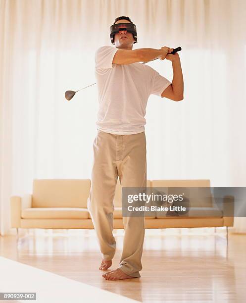 young man wearing virtual reality goggles while playing golf in home - golf simulator stock pictures, royalty-free photos & images