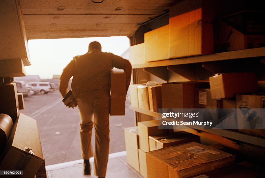 Delivery man exiting truck with package, rear view