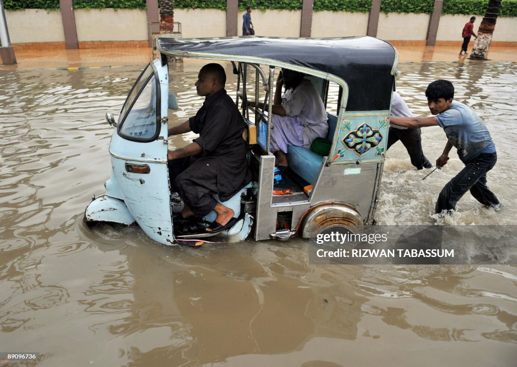 Pakistani push a stranded auto-rickshaw along a flooded street after ...
