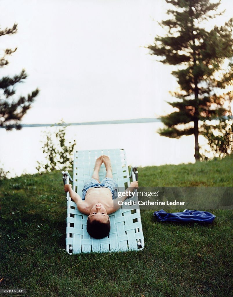 Boy (6-8) lying on lounger by lake