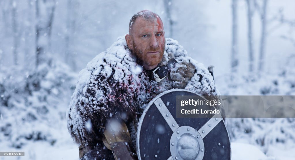 Schwert schwingende blutigen Wikinger Krieger versteckt hinter seinem Schild in einem Schneesturm winter