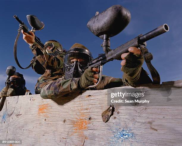 paint ball battle, players in camouflage aiming guns - paintball stock pictures, royalty-free photos & images