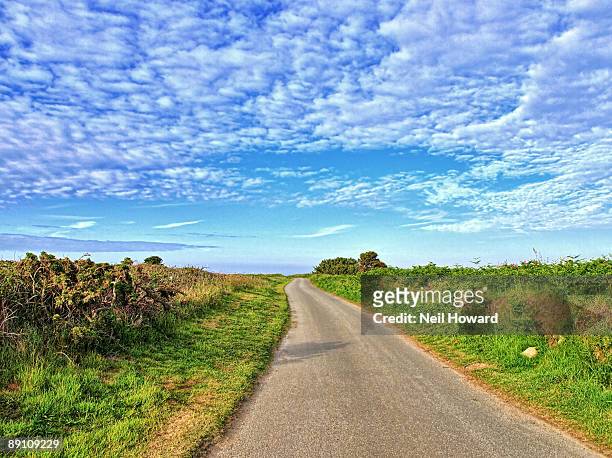 a lonely country road under puffy clouds - island of alderney photos et images de collection