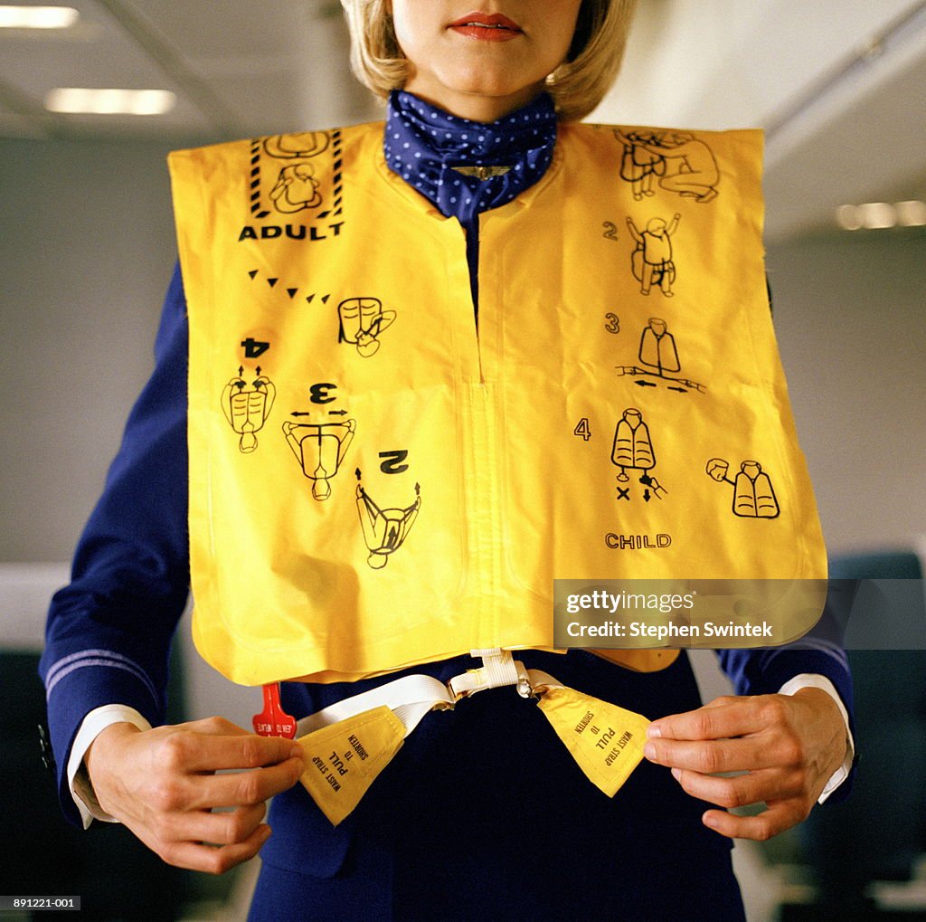 Flight attendant demonstrating how to use emergency vest on airliner