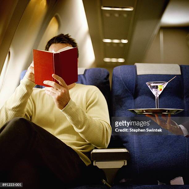man reading book, being served martini, in first class on airliner - banco de avião imagens e fotografias de stock