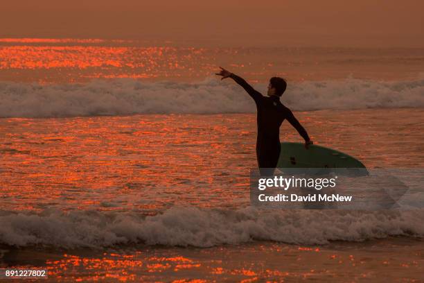 Smoke-filled sky filters sunlight to orange around a surfer as the Thomas Fire continues to grow and threaten communities from Carpinteria to Santa...