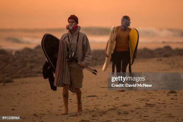 Smoke-filled sky filter orange light around surfers as the Thomas Fire continues to grow and threaten communities from Carpinteria to Santa Barbara...