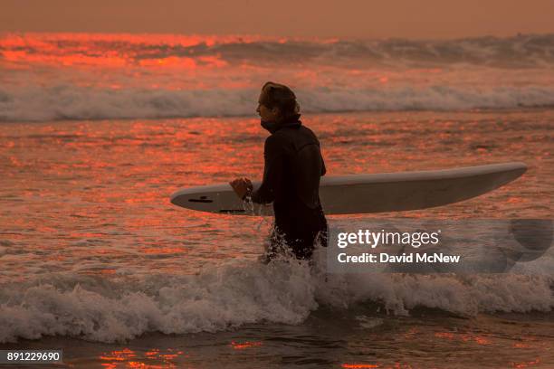 Smoke-filled sky filters sunlight to orange around a surfer as the Thomas Fire continues to grow and threaten communities from Carpinteria to Santa...