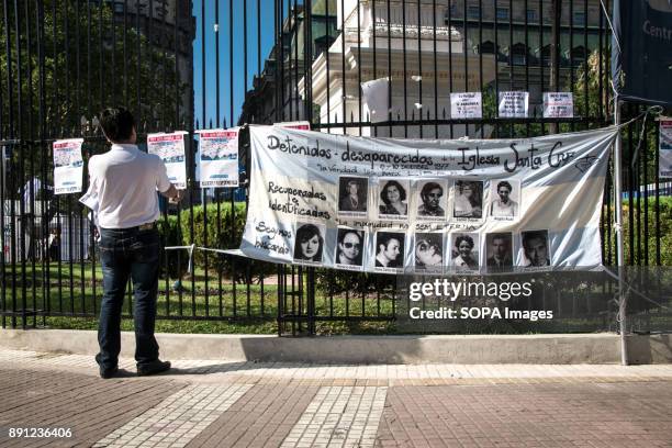 Spectator reads posters listing the names of disappeared citizens near a large banner with photographs of the disappeared. The 'Madres' of Plaza de...
