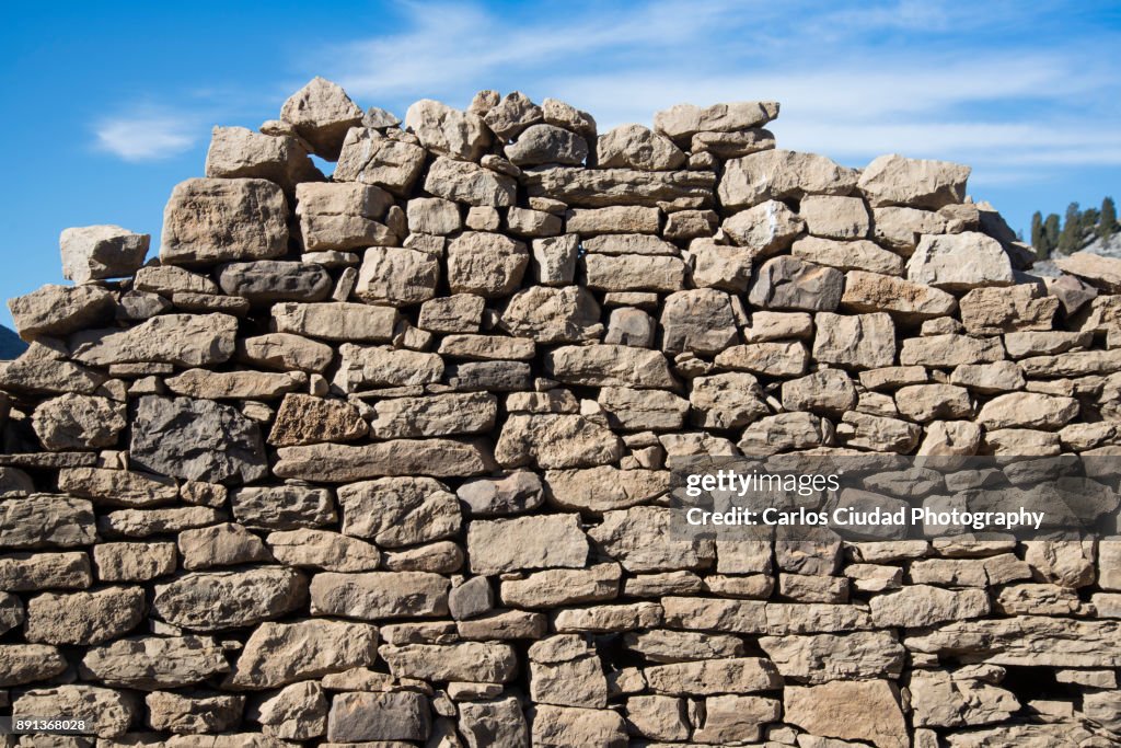 Collapsed dry stone wall against blue sky