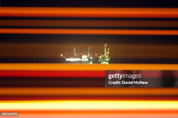 The lights of cars and trucks traveling on Highway 101 streak past distant offshore oil rigs that are extracting crude oil used to power some of...