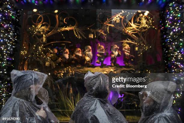 Pedestrians wearing plastic ponchos pass in front of a holiday window display at the Saks Fifth Avenue Inc. Department store in New York, U.S., on...