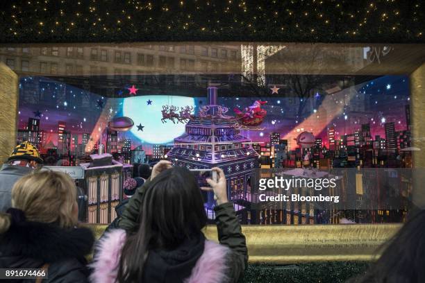 Pedestrian uses a mobile device to take photographs of a the holiday window display at the Macy's Inc. Department store in New York, U.S., on Sunday,...