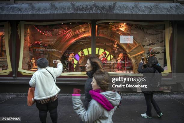 Pedestrians use mobile devices to take photographs of a holiday window display at the Macy's Inc. Department store in New York, U.S., on Saturday,...