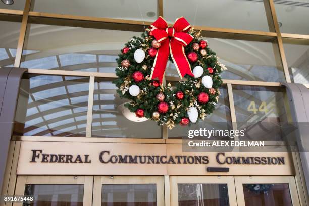 Holiday wreath hangs over the front entrance of the Federal Communications Commission headquarters building while a demonstration takes place across...