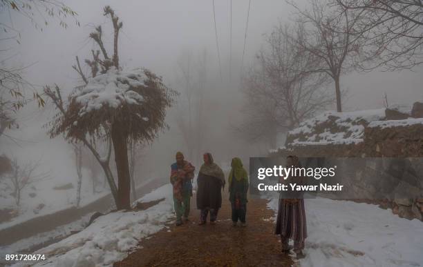 Kashmiris walk on a snow cleared road amid dense fog after seasons first snowfall on December 13, 2017In the outskirts of Srinagar, the summer...