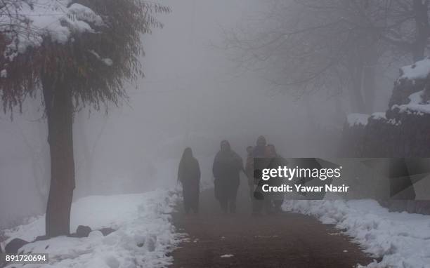 Kashmiris walk on a snow cleared road amid dense fog after seasons first snowfall on December 13, 2017In the outskirts of Srinagar, the summer...