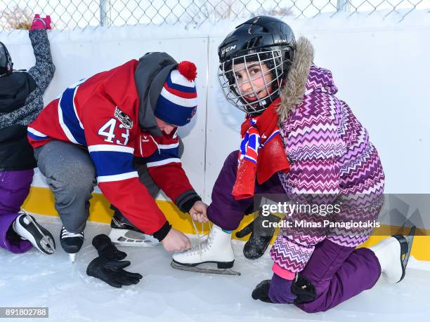 Daniel Carr of the Montreal Canadiens helps a young girl tie her skates during the official inauguration of the Bleu Blanc Bouge rink by the Montreal...