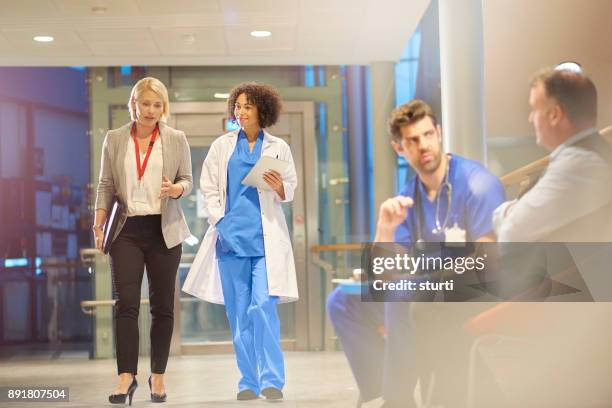 doctor listening to sales rep in hospital corridor - medical partnership stock pictures, royalty-free photos & images