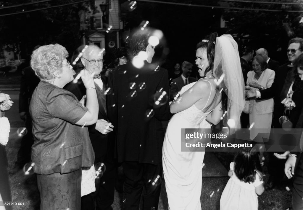 Bride and groom leaving ceremony, guests blowing bubbles (B&W)