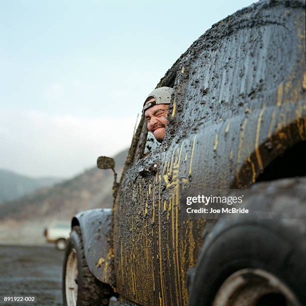 man in yellow car covered in mud, side view - dirty car stock-fotos und bilder