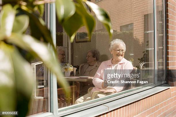 elderly women sitting in nursing home window - senior care stock pictures, royalty-free photos & images