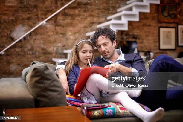 father helping daughter with homework on couch - black hair stockfoto's en -beelden