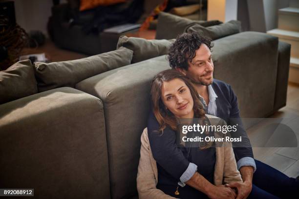 smiling couple sitting in living room leaning against couch - straight black hair stock pictures, royalty-free photos & images