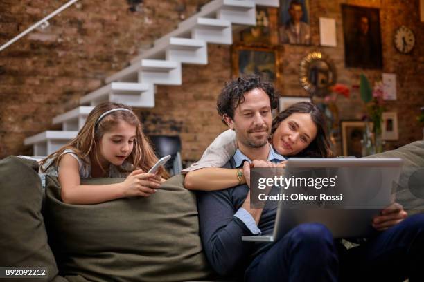 family on couch at home using technology - lifestyles stock photos et images de collection