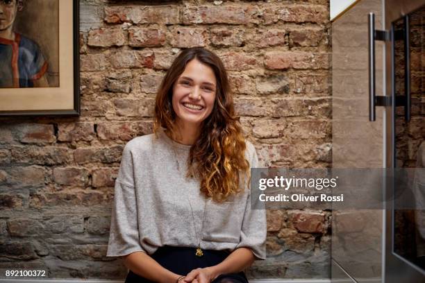 portrait of happy brunette woman in front of brick wall at home - wavy brown hair stock pictures, royalty-free photos & images