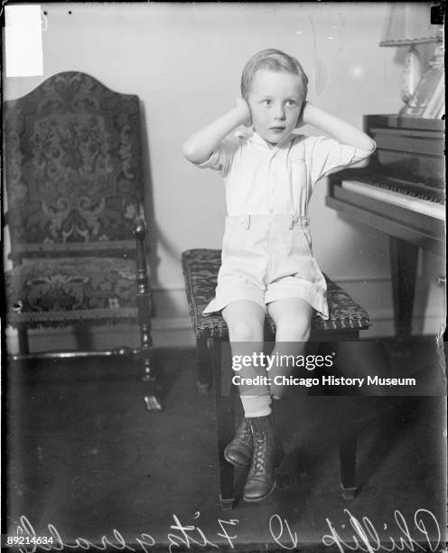 Full-length portrait of Phillip D. Fitzgerald, a boy shaken by a bomb explosion, holding his hands over his ears, sitting at a piano in a room in...