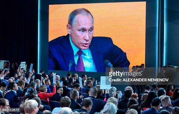 Video screen displays Russian President Vladimir Putin speaking during his annual press conference in Moscow while journalists hold placards, on...