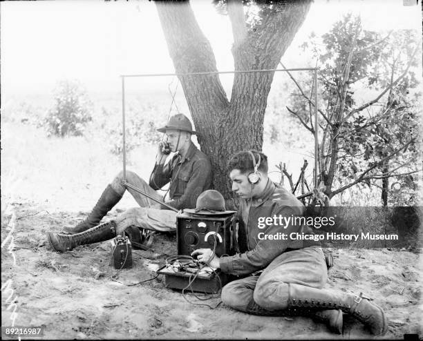 Informal full-length portrait of two soldiers in the 122nd Field Artillery Regiment sitting outdoors next to a portable radio device at Camp McCoy in...