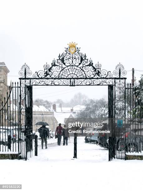 people walking through the entrance gates of cirencester park, gloucestershire, the cotswolds down cecily hill towards cirencester town centre on a snowy december day 2017 - cotswolds stock pictures, royalty-free photos & images