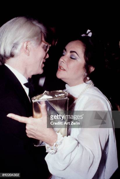 American Artist Andy Warhol embraces actress Elizabeth Taylor as she clutches her purse with her eyes closed at an event, New York City, 1970.