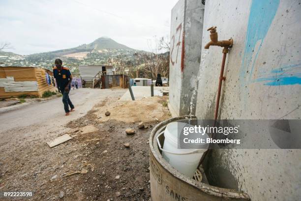 Communal water taps runs to fill a plastic container underneath in the Imizamo Yethu township outside Cape Town, South Africa on Monday, Nov. 13,...