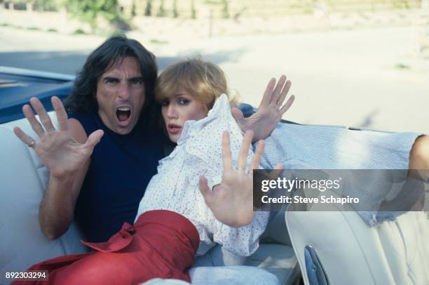 View of American musician Alice Cooper and his wife, choreographer Sheryl Cooper as they hold out their palms from the back seat of a convertible,...