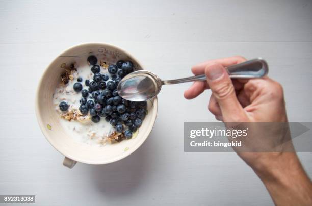 mano con cucchiaio che raggiunge i cereali per la colazione con mirtilli e latte - cucchiaio foto e immagini stock