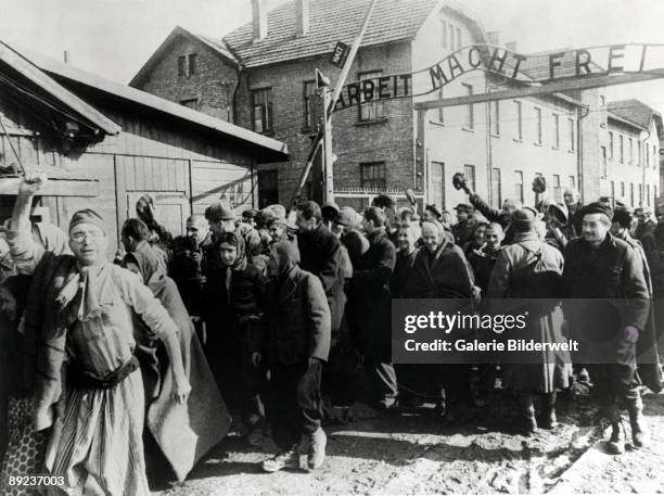 Survivors of Auschwitz leaving the camp at the end of World War II, Poland, February 1945. Above them is the German slogan 'Arbeit macht frei' ....