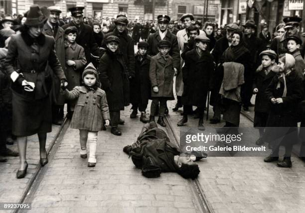 Passers-by ignore a man lying in the street in the Warsaw Ghetto, Poland, 1941. The scene was possibly arranged.