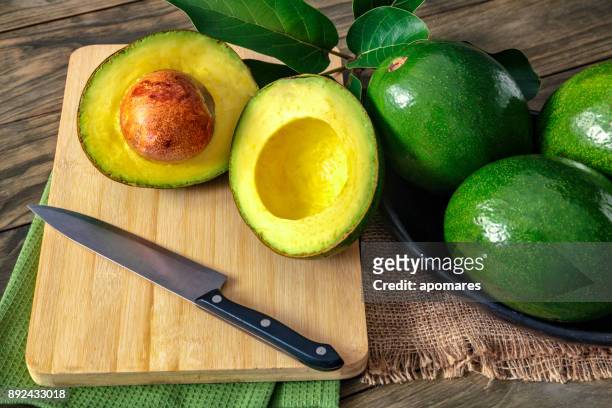 nahaufnahme eines grünen reife avocados mit blättern - aguacates stock-fotos und bilder