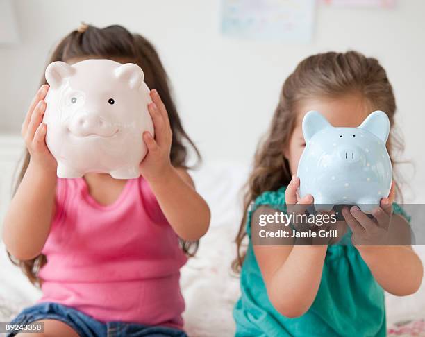 two girls holding piggy banks - spardose stock-fotos und bilder